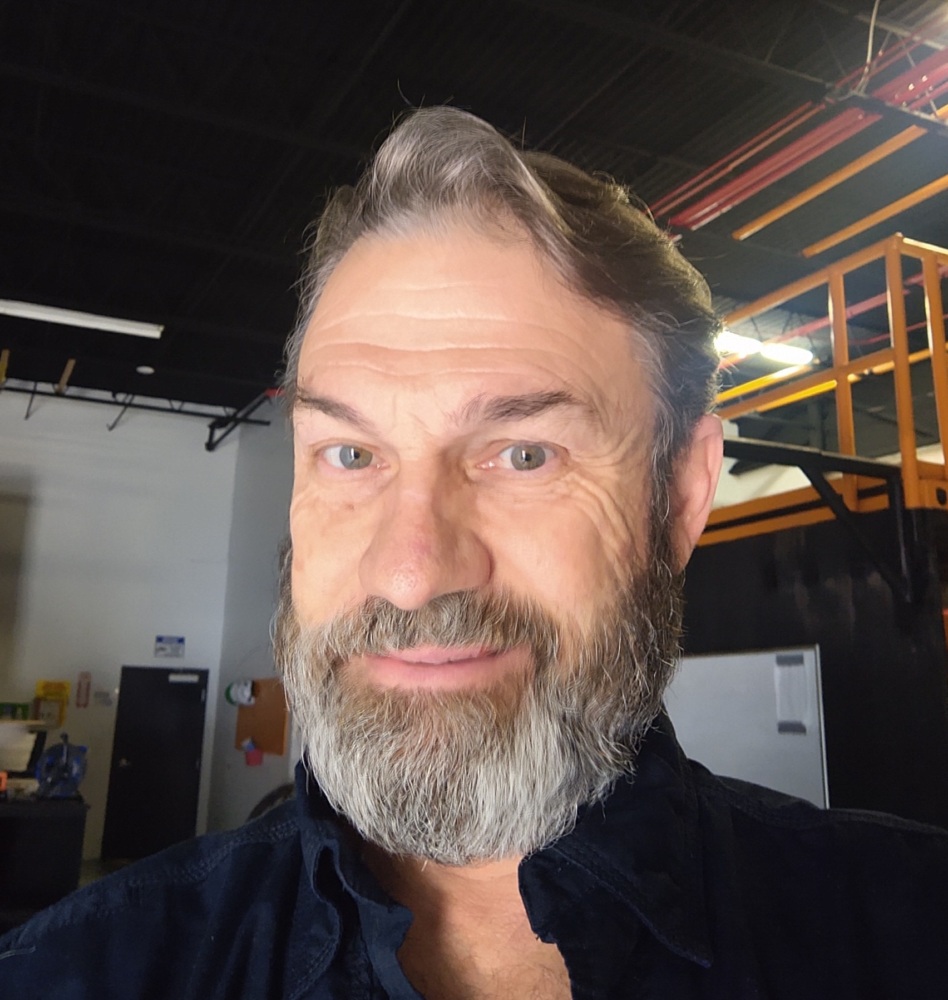A man with a beard taking a selfie in a warehouse.